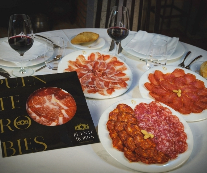Mesa con platos de embutidos y frutos secos con pan en recipiente separado y vino