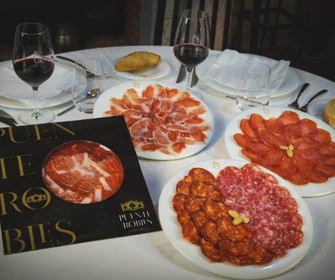 Mesa con platos de embutidos y frutos secos con pan en recipiente separado y vino