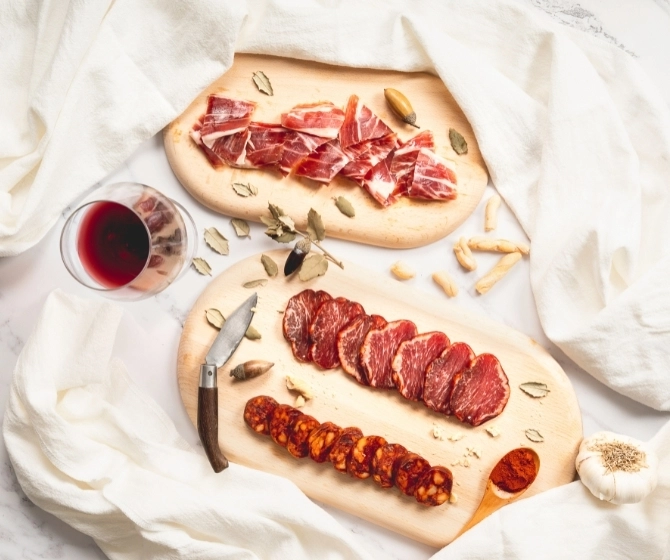 Presentación y decoración de los embutidos en una tabla de madera con vino y detalles decorativos.